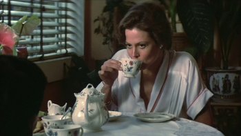 Movie still from “The Year of Living Dangerously” (1982), directed by Peter Weir – A woman sitting at a table drinking from a tea cup; Medium shot, High angle
