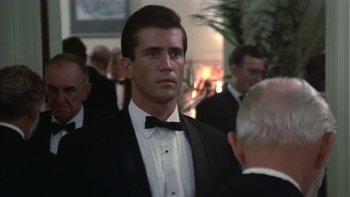 Movie still from “The Year of Living Dangerously” (1982), directed by Peter Weir – A man in a suit and bow tie standing in front of a crowd; Close Up shot, Over the shoulder angle