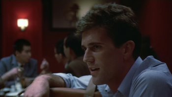 Movie still from “The Year of Living Dangerously” (1982), directed by Peter Weir – A person sitting at a table; Close Up shot, Over the shoulder angle