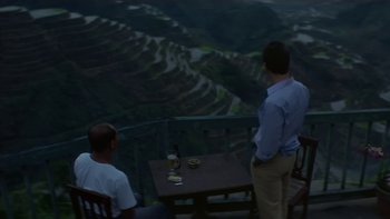 Movie still from “The Year of Living Dangerously” (1982), directed by Peter Weir – Two men standing at a table with a bottle of wine; Extreme Wide shot, High angle