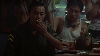 Movie still from “The Year of Living Dangerously” (1982), directed by Peter Weir – A man sitting at a table smoking a cigarette; Medium shot, Over the shoulder angle
