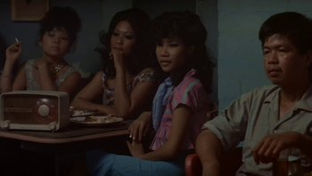 Movie still from “The Year of Living Dangerously” (1982), directed by Peter Weir – A group of people sitting around a table; Medium shot, Over the shoulder angle