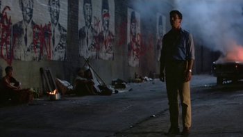 Movie still from “The Year of Living Dangerously” (1982), directed by Peter Weir – A man standing on the side of the road near a wall; Wide shot, Low angle