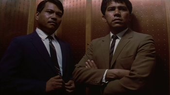 Movie still from “The Year of Living Dangerously” (1982), directed by Peter Weir – A couple of men standing next to each other in suits; Medium shot, Low angle