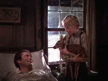 Movie still from “The Yearling” (1946), directed by Clarence Brown – A man and a boy with a deer in a room; Medium shot, High angle