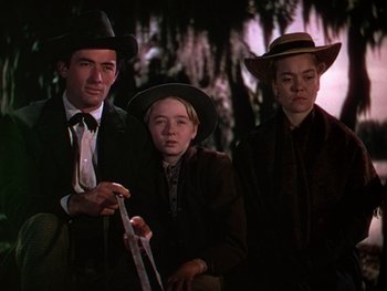 Movie still from “The Yearling” (1946), directed by Clarence Brown – A man and two young women in hats and suits; Medium shot, Low angle