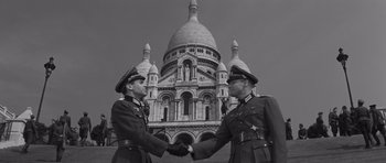 Movie still from “The Young Lions” (1958), directed by Edward Dmytryk – Two men in military uniforms shaking hands in front of a building; Wide shot, Low angle