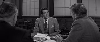 Movie still from “The Young Lions” (1958), directed by Edward Dmytryk – A man sitting at a table in front of two other people; Medium shot, Over the shoulder angle