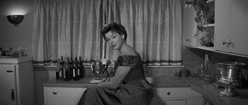 Movie still from “The Young Lions” (1958), directed by Edward Dmytryk – A black and white photo of a woman sitting at a table with a glass of wine; Medium shot, Low angle