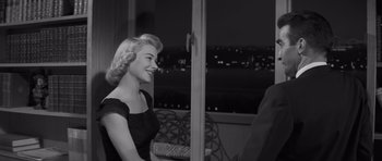 Movie still from “The Young Lions” (1958), directed by Edward Dmytryk – A woman sitting in front of a window with a city view; Medium shot, Over the shoulder angle