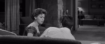 Movie still from “The Young Lions” (1958), directed by Edward Dmytryk – A woman and a man sitting on a couch in a living room; Medium shot, Over the shoulder angle