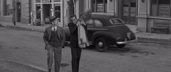Movie still from “The Young Lions” (1958), directed by Edward Dmytryk – Two men are walking down the street in front of an old car; Wide shot, Low angle