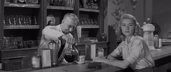 Movie still from “The Young Lions” (1958), directed by Edward Dmytryk – An older man pouring a drink into a glass; Medium shot, Over the shoulder angle