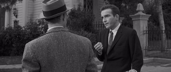 Movie still from “The Young Lions” (1958), directed by Edward Dmytryk – A man in a suit talks to another man in a hat; Medium shot, Over the shoulder angle