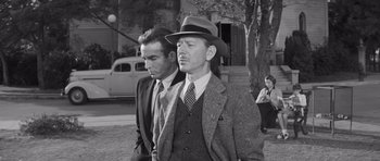 Movie still from “The Young Lions” (1958), directed by Edward Dmytryk – A man in a suit and a man in a hat and tie; Medium shot, Low angle