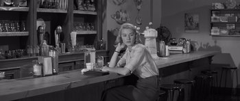 Movie still from “The Young Lions” (1958), directed by Edward Dmytryk – A black and white photo of a woman sitting at a bar; Medium shot, Low angle