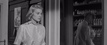 Movie still from “The Young Lions” (1958), directed by Edward Dmytryk – A black - and - white photo of a woman standing in front of a door; Medium shot, Low angle
