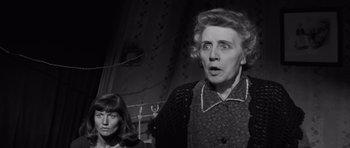 Movie still from “The Young Lions” (1958), directed by Edward Dmytryk – A woman and an older woman are standing in a dark room; Medium shot, Low angle