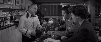 Movie still from “The Young Lions” (1958), directed by Edward Dmytryk – Two men sitting at a table in front of a bar; Medium shot, Over the shoulder angle