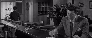 Movie still from “The Young Lions” (1958), directed by Edward Dmytryk – A man sitting at a bar with a glass of water; Medium shot, Over the shoulder angle