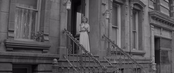 Movie still from “The Young Lions” (1958), directed by Edward Dmytryk – A black and white photo of a woman standing on the steps of a building; Wide shot, Low angle