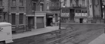 Movie still from “The Young Lions” (1958), directed by Edward Dmytryk – A person walking on a sidewalk in front of a building; Extreme Wide shot, High angle