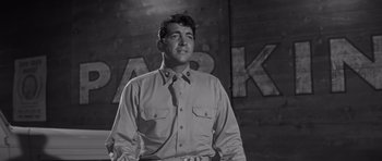Movie still from “The Young Lions” (1958), directed by Edward Dmytryk – Black and white photograph of a man standing in front of a parking sign; Medium shot, Low angle