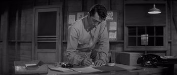 Movie still from “The Young Lions” (1958), directed by Edward Dmytryk – A black and white photo of a man writing on a piece of paper; Medium shot, High angle