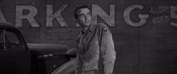 Movie still from “The Young Lions” (1958), directed by Edward Dmytryk – Black and white photograph of a man standing in front of a motorcycle; Medium shot, Low angle