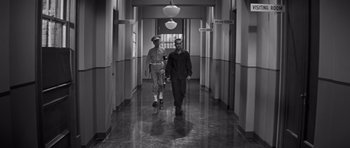 Movie still from “The Young Lions” (1958), directed by Edward Dmytryk – A man and a woman are walking down a hallway; Wide shot, High angle