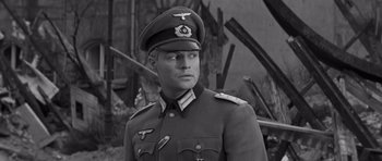 Movie still from “The Young Lions” (1958), directed by Edward Dmytryk – A man in a military uniform is standing in front of a wall; Medium shot, High angle