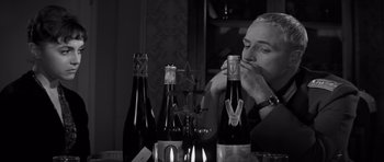 Movie still from “The Young Lions” (1958), directed by Edward Dmytryk – A black and white photo of a man sitting at a table with several bottles of wine; Close Up shot, Low angle