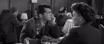 Movie still from “The Young Lions” (1958), directed by Edward Dmytryk – A man sitting at a table smoking a cigarette in front of a woman; Medium shot, Over the shoulder angle