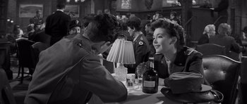 Movie still from “The Young Lions” (1958), directed by Edward Dmytryk – A group of people sitting at a table with drinks; Medium shot, Over the shoulder angle