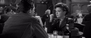 Movie still from “The Young Lions” (1958), directed by Edward Dmytryk – A man and a woman are sitting at a table; Medium shot, Over the shoulder angle