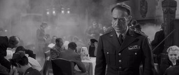 Movie still from “The Young Lions” (1958), directed by Edward Dmytryk – A man in a uniform standing in front of a group of people; Medium shot, Over the shoulder angle