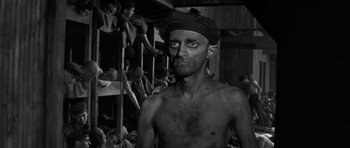 Movie still from “The Young Lions” (1958), directed by Edward Dmytryk – An old man with no shirt is standing in front of a group of people; Medium shot, Low angle