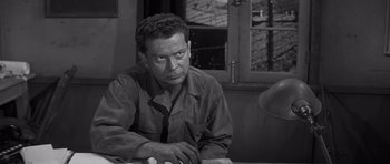 Movie still from “The Young Lions” (1958), directed by Edward Dmytryk – A black and white photo of a man sitting at a table; Close Up shot, High angle