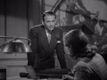 Movie still from “The Young in Heart” (1938), directed by Gilbert Pratt – A man standing in front of a woman in front of a desk; Medium shot, Over the shoulder angle