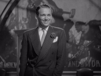 Movie still from “The Young in Heart” (1938), directed by Gilbert Pratt – A man in a suit and tie smiling for the camera; Medium shot, Low angle