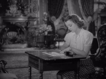 Movie still from “The Young in Heart” (1938), directed by Gilbert Pratt – A woman sitting at a table looking down at a piece of paper; Medium shot, High angle