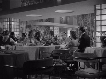Movie still from “The Young in Heart” (1938), directed by Gilbert Pratt – A group of people sitting at tables in a room; Wide shot, High angle