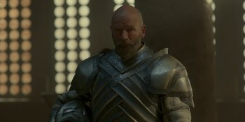 Movie still from “House of the Dragon” (2022), created by George R.R. Martin – A bald man in a suit of armor and holding a sword; Medium shot, Over the shoulder angle