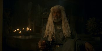 Movie still from “House of the Dragon” (2022), created by George R.R. Martin – A man sitting in a chair wearing a dreadlock wig; Medium shot, Low angle