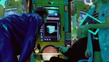 Movie still from “The Zero Theorem” (2013), directed by Terry Gilliam – Two people are playing a video game on a big screen; Medium shot, Over the shoulder angle