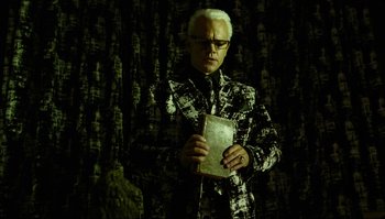 Movie still from “The Zero Theorem” (2013), directed by Terry Gilliam – A man in a suit and tie holding a book; Medium shot, Low angle