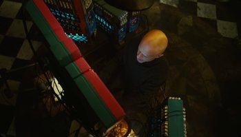 Movie still from “The Zero Theorem” (2013), directed by Terry Gilliam – A man with a bald head standing in front of a computer; Medium shot, Overhead angle