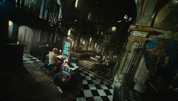 Movie still from “The Zero Theorem” (2013), directed by Terry Gilliam – A man sitting at a table in an abandoned building; Extreme Wide shot, High angle