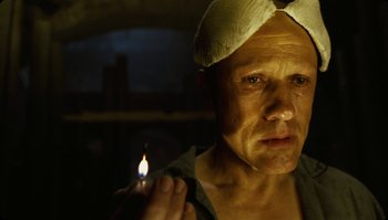 Movie still from “The Zero Theorem” (2013), directed by Terry Gilliam – A man holding a lit candle in a dark room; Close Up shot, Low angle