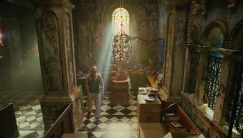 Movie still from “The Zero Theorem” (2013), directed by Terry Gilliam – A man standing in the middle of a room with sunlight coming through the window; Wide shot, Low angle